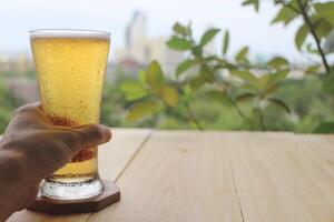 birra nel un' chiaro bicchiere su un' di legno tavolo. persone siamo Tenere un' bicchiere di birra. foto