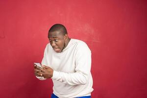 felicissimo africano uomo utilizzando smartphone gli sport scommesse, vincere i soldi isolato su rosso sfondo. foto