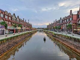 Giacarta, Indonesia - gennaio 30 2024 negozi su il bordo di il fiume con Barche passaggio di con edifici con un' poco europeo amsterdam foto