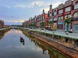 Giacarta, Indonesia - gennaio 30 2024 negozi su il bordo di il fiume con Barche passaggio di con edifici con un' poco europeo amsterdam foto