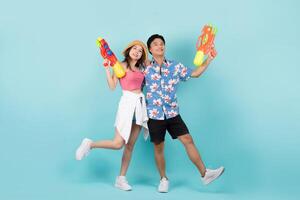 pieno corpo tiro di contento giovane asiatico coppia nel estate abiti con acqua pistola e guardare a telecamera nel blu sfondo. foto