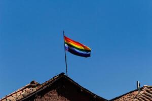 cusco, Perù, 2015 - arcobaleno bandiera contro blu cielo su rosso piastrella tetto Sud America foto