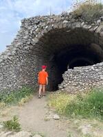 un' bambino nel un arancia camicia è in piedi nel davanti di un' pietra tunnel foto