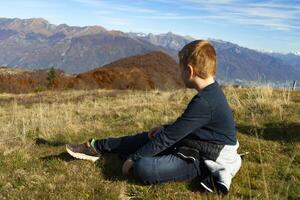 un' ragazzo seduta su il terra nel davanti di montagne foto