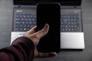 mano utilizzando un cellulare moderno e uno sfondo per laptop
