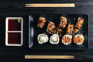 rotoli di sushi con le bacchette e salsa di soia sul tavolo scuro. vista dall'alto foto