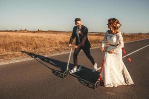 sposi sorridenti in sella a uno scooter lungo la strada fuori città al tramonto foto