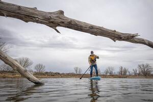 anziano maschio paddling un' In piedi su paddleboard su un' lago nel presto molla, rana prospettiva a partire dal un azione telecamera a acqua livello foto