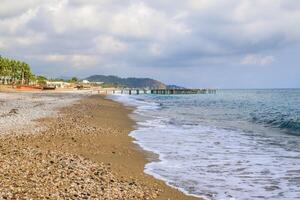 tranquillo ciottolo spiaggia e molo su nuvoloso giorno, ideale individuare per sereno riva del mare passeggiare foto