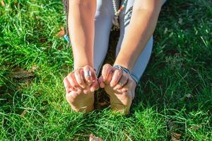 vicino su mani e gambe di donna fare yoga esercizio su un' erba nel un' parco. concetto di salutare stile di vita. foto