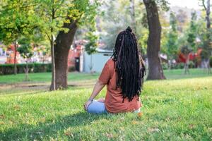 bellissimo giovane donna con lungo africano trecce è fare yoga al di fuori nel un' parco. concetto di salutare stile di vita. foto