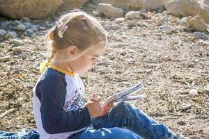 giovane ragazza godendo un' tranquillo, calmo momento di il lago mentre immersa nel un' travolgente libro foto