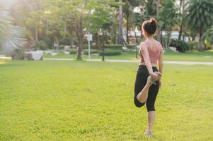 femmina jogging, in forma 30s giovane asiatico donna nel rosa abbigliamento sportivo, caldo su corpo nel parco prima correre. salutare all'aperto stile di vita fitness corridore ragazza contro tramonto. benessere e benessere concetto. foto