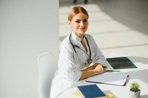 femmina medico Lavorando a ufficio scrivania e sorridente, ufficio interno su sfondo foto