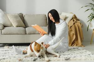 ragazza lettura un' libro con sua cane accanto suo. donna legge un' libro con cane su il pavimento foto