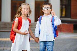 contento bambini - ragazzo e ragazza con libri e zaini su il primo scuola giorno. eccitato per essere indietro per scuola dopo vacanza. pieno lunghezza all'aperto ritratto. foto