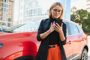 donna utilizzando mobile Telefono, comunicazione o in linea applicazione, in piedi vicino auto su città strada o parcheggio, all'aperto. auto condivisione, noleggio servizio o Taxi app. foto