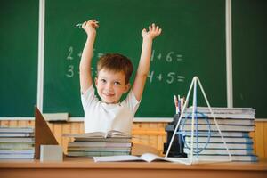 indietro per scuola. divertente scolaro seduta a un' tavolo con libri nel un' scuola aula. foto