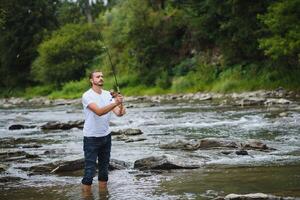 barbuto uomo attraente pesce. estate tempo libero. maturo uomo pesca su il stagno. ritratto di allegro anziano uomo pesca. maschio pesca. pescatore uncinetto rotazione in il fiume in attesa grande pesce foto