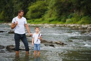 padre e figlio pesca. padre con il suo figlio su il fiume godendo pesca Tenere pesca canne foto