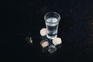 Vodka tiro con ghiaccio su nero tavolo, copia spazio. foto