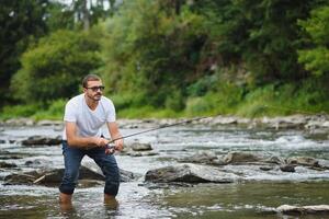 barbuto uomo attraente pesce. estate tempo libero. maturo uomo pesca su il stagno. ritratto di allegro anziano uomo pesca. maschio pesca. pescatore uncinetto rotazione in il fiume in attesa grande pesce foto