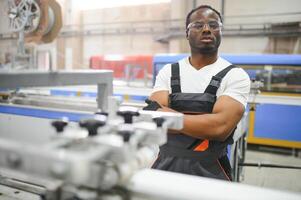 ritratto di africano americano maschio ingegnere nel uniforme e in piedi nel industriale fabbrica foto