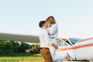 contento giovane coppia ridendo e avendo divertimento su pista di decollo vicino privato aereo foto