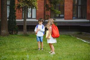 contento bambini partire indietro per scuola. allievo di primario scuola partire studia con zaino all'aperto. bambini partire mano nel mano. inizio di Lezioni. primo giorno di autunno. ragazzo e ragazza a partire dal elementare alunno. foto