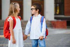 contento bambini - ragazzo e ragazza con libri e zaini su il primo scuola giorno. eccitato per essere indietro per scuola dopo vacanza. pieno lunghezza all'aperto ritratto. foto