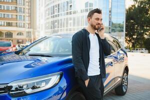 un' bello giovane uomo d'affari in piedi Il prossimo per il suo auto e parlando su il suo Telefono foto