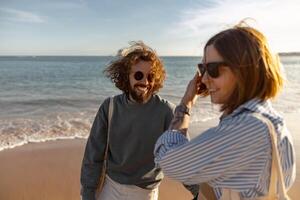 sorridendo coppia nel amore scemo in giro mentre a piedi lungo il spiaggia su soleggiato ventoso giorno foto