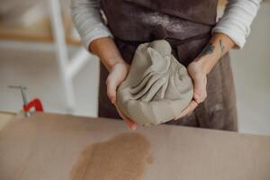 vicino su di donna preparazione argilla per creare un' boccale su un' di legno tavolo nel ceramica studio foto