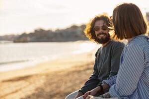 sorridente romantico coppia seduta a il spiaggia indossare casuale Abiti e guardare ogni altro foto