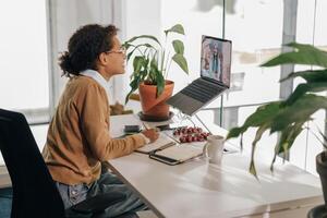 femmina libero professionista avere video conferenza con cliente e fabbricazione Appunti seduta nel accogliente coworking foto