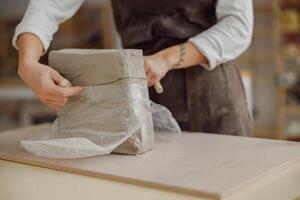 vicino su di ceramista donna indossare grembiule è preparazione argilla per rendere ceramica pezzi nel sua studio foto