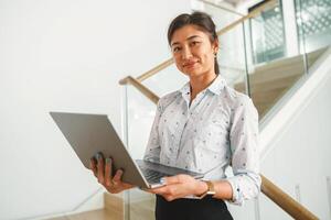 sorridente donna manager in piedi con il computer portatile e guardare a telecamera su coworking sfondo foto