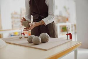 vicino su di ceramista donna indossare grembiule è preparazione argilla per rendere ceramica pezzi nel sua studio foto