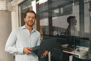 bello libero professionista con il computer portatile in piedi su moderno coworking sfondo e guardare a telecamera foto