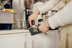 avvicinamento di barista utilizzando un' manomettere per stampa terra caffè in un' portafilter a il caffè negozio foto