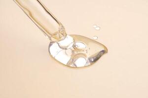 un' cosmetico Prodotto gel o collagene siero flussi su di un' pipetta con bolle su beige sfondo. foto