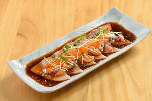 pesce hamachi carpaccio con chili salsa nel un' bianca vassoio su di legno sfondo superiore Visualizza di giapponese cibo foto