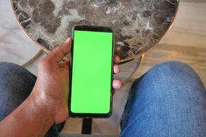 primo piano della mano del giovane che utilizza lo smartphone con lo schermo verde foto