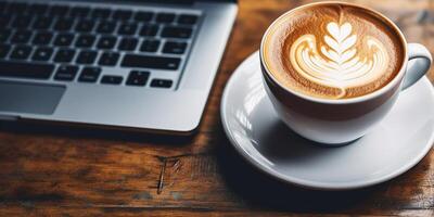 ai generato avvicinamento di un' tazza di caldo latte macchiato caffè con un' latte schiuma modello e un' il computer portatile su un' di legno tavolo foto