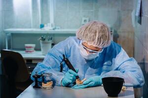 un' dentale tecnico nel protettivo capi di abbigliamento è Lavorando su un' protesico dente nel il suo laboratorio foto