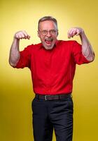 divertente anziano uomo mostrando il muscoli con Aperto bocca sorridente allegramente al di sopra di giallo sfondo foto