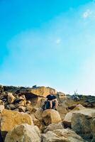un' riposo giovane turista seduta su il sfondo di il roccia e guardare dritto avanti. turismo nel un' caldo estate giorno. foto