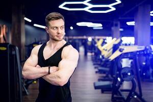 uomo con atletico corpo in piedi nel il palestra. fiducioso muscolare allenatore su il palestra. foto