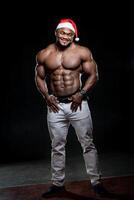 afro americano atletico uomo nel Santa cappello sta con mano nel tasca. molto muscolare corpo e forte addominali. foto