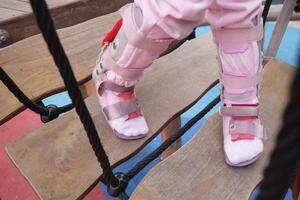 un' poco ragazza nel ortesi scarpe croci un' di legno ponte bambino cerebrale paralisi disabilità. foto
